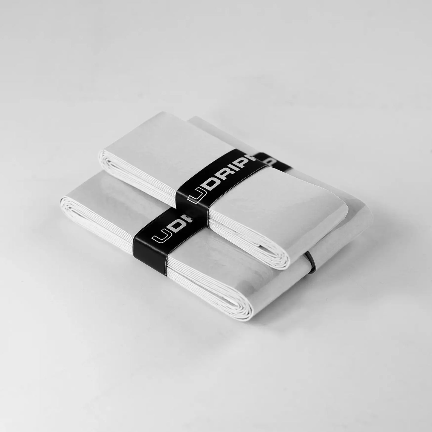 Two stacks of UDRIPPIN Pro Tour Extra Tacky Overgrips, secured with black bands on a gray surface.