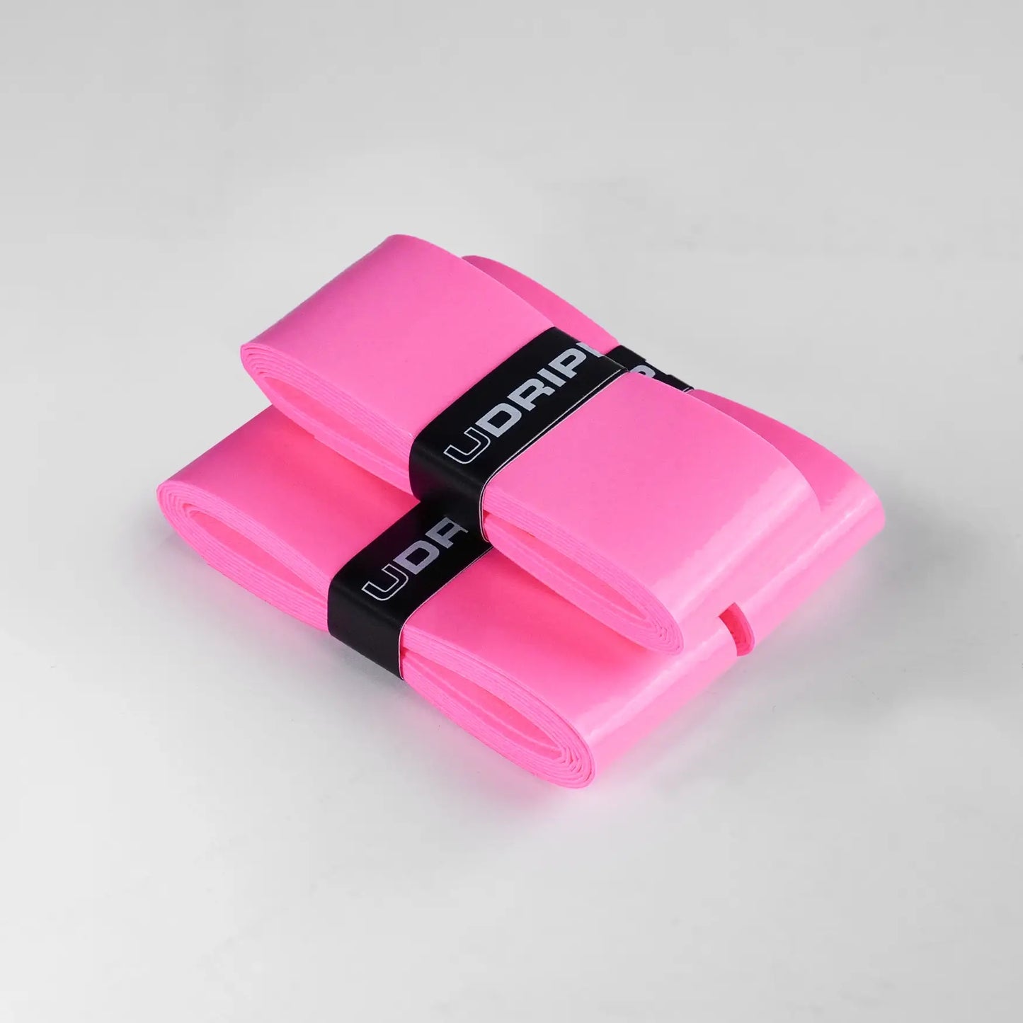 Two neatly folded neon pink UDRIPPIN Comfort Tour Overgrips, secured with a black band labeled "UDRIP," on a plain gray background.