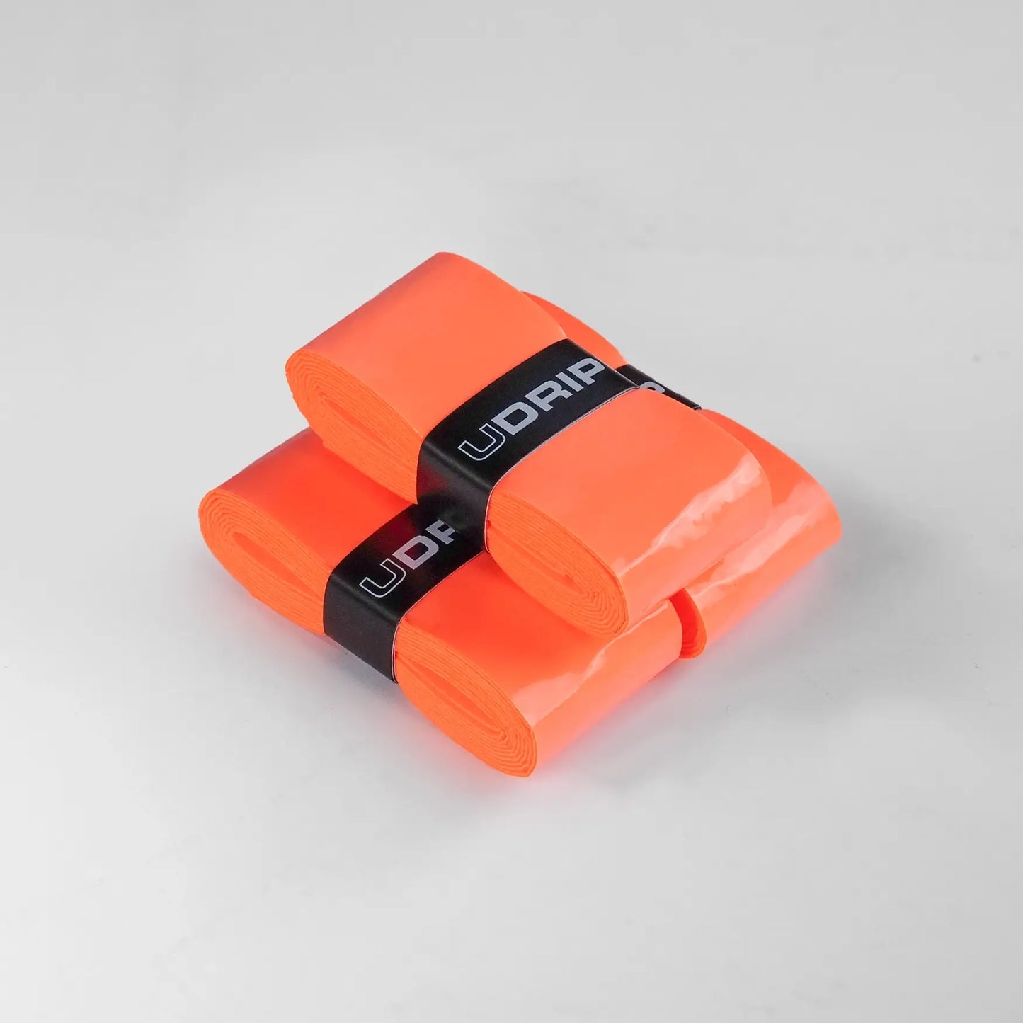 Two sets of vibrant orange UDRIPPIN Comfort Tour Overgrips are arranged on a light gray surface.