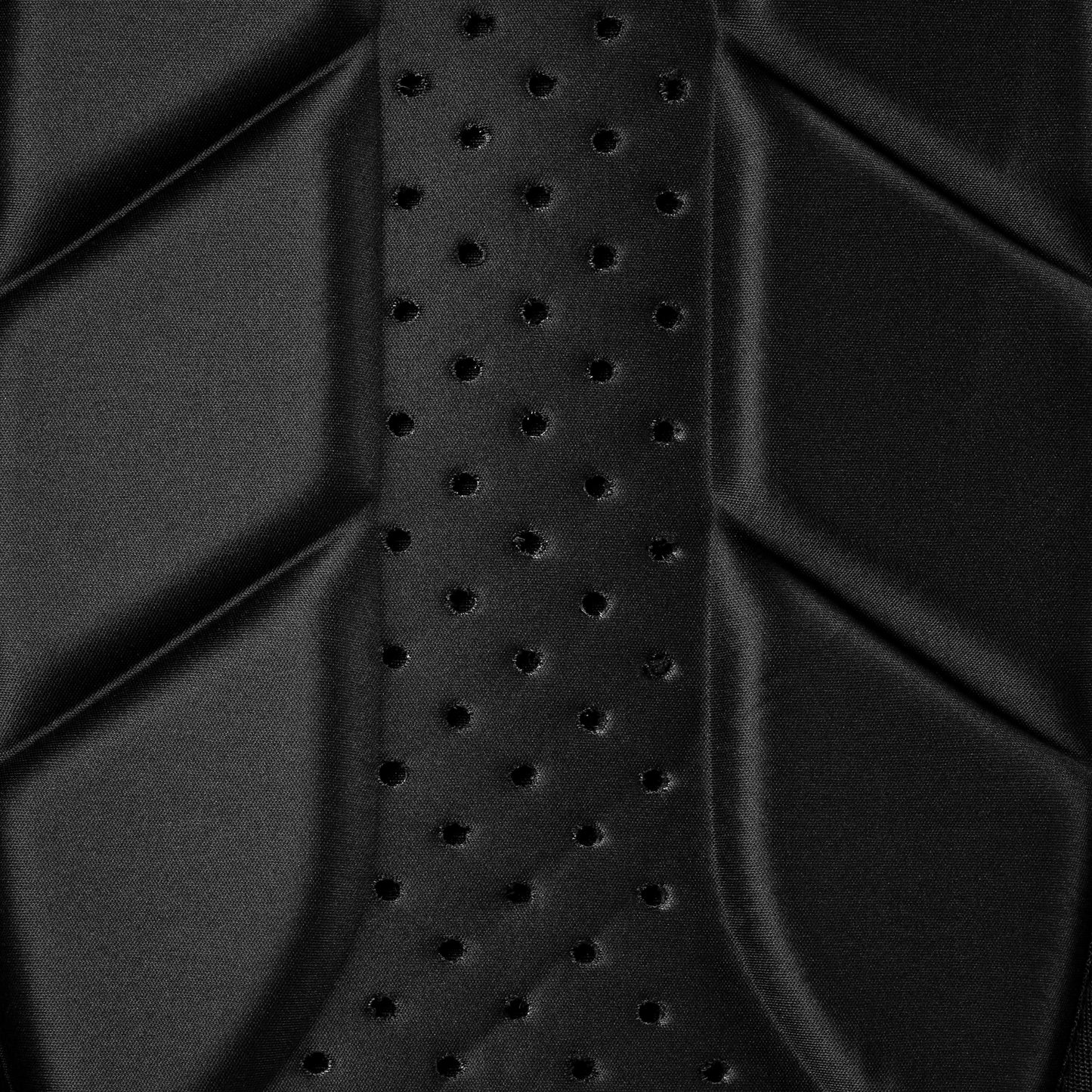 Close-up of a black, textured surface with geometric patterns and a series of small perforations in the center of the Selkirk Core Series Tour Backpack Pickleball Bag by Selkirk.
