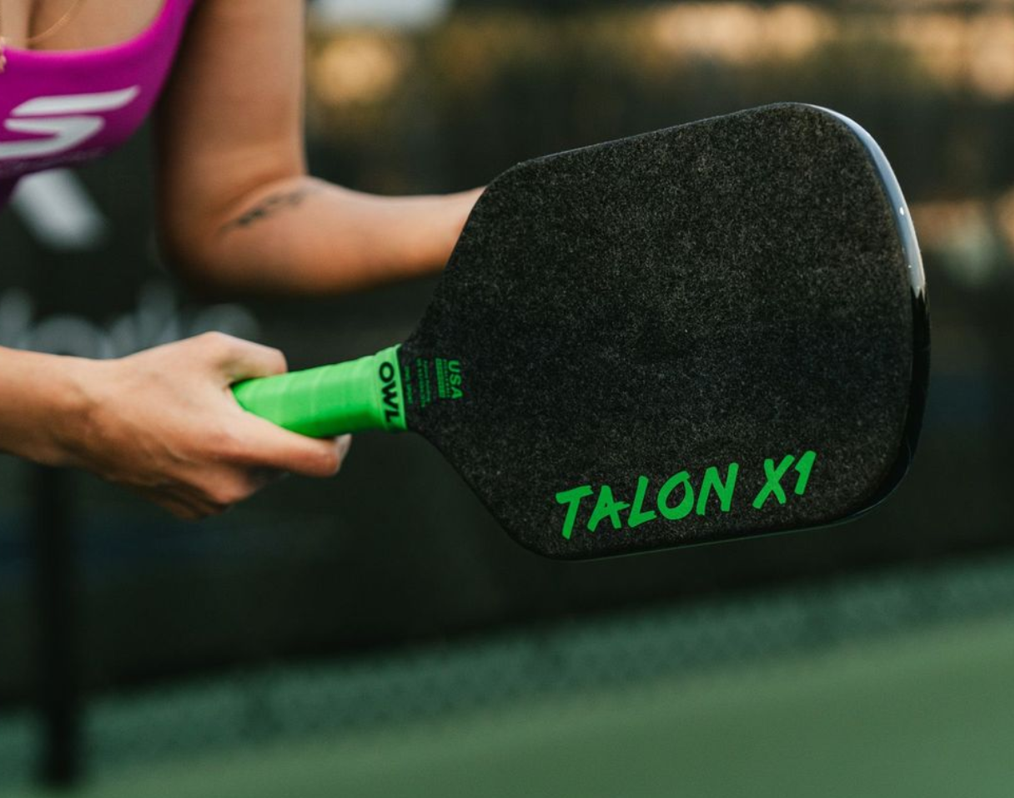 A player holds an OWL Talon X1 Quiet Pickleball Paddle, black with a green grip and advanced spin control, standing on an outdoor court.