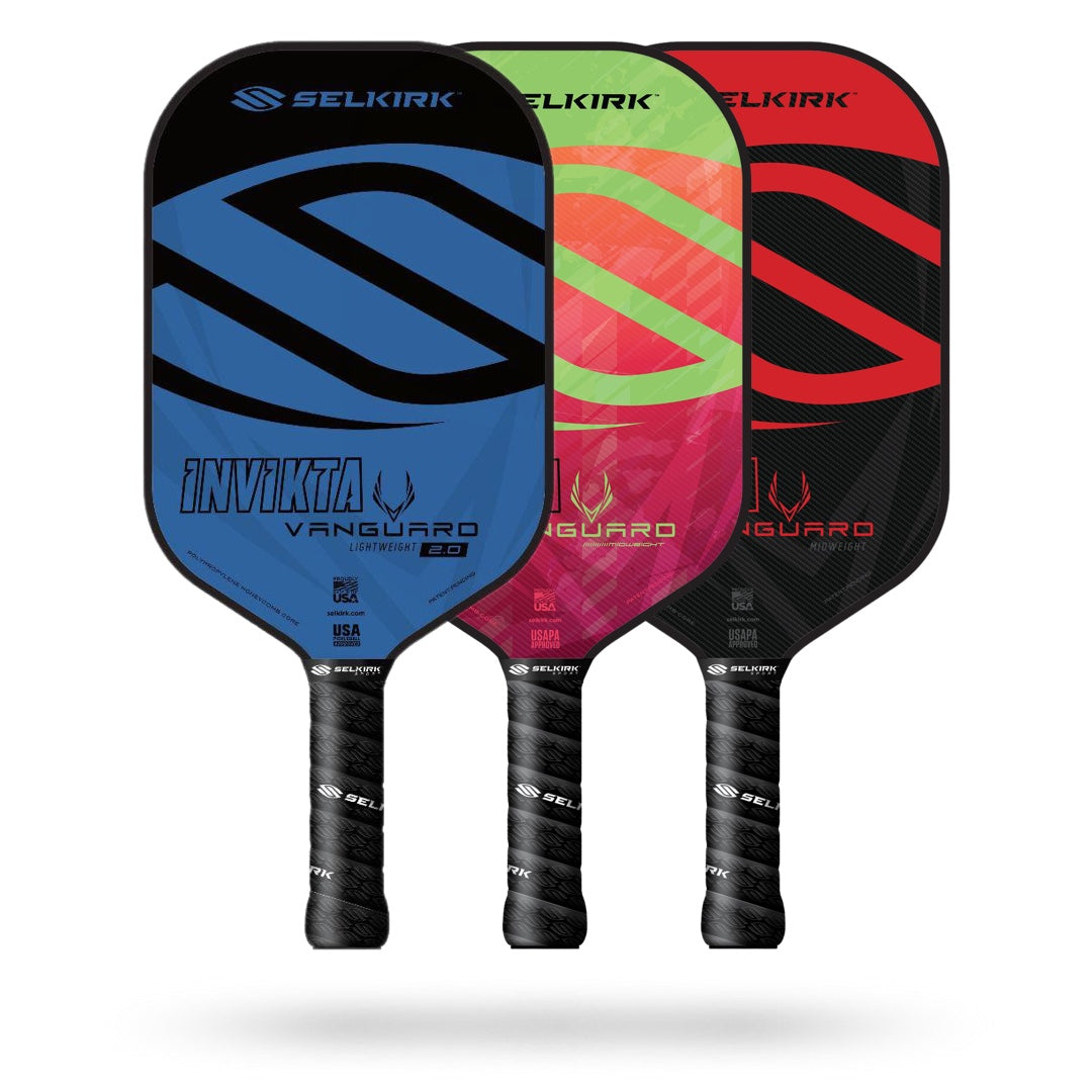 Three Selkirk pickleball paddles are shown: a blue Selkirk Vanguard Invikta Pickleball Paddle, a green Selkirk Vanguard Invikta Pickleball Paddle, and a red Selkirk Vanguard Invikta Pickleball Paddle. They stand upright with black handles at the bottom and the Selkirk logo prominently displayed. Each paddle comes with a limited lifetime warranty for your peace of mind.