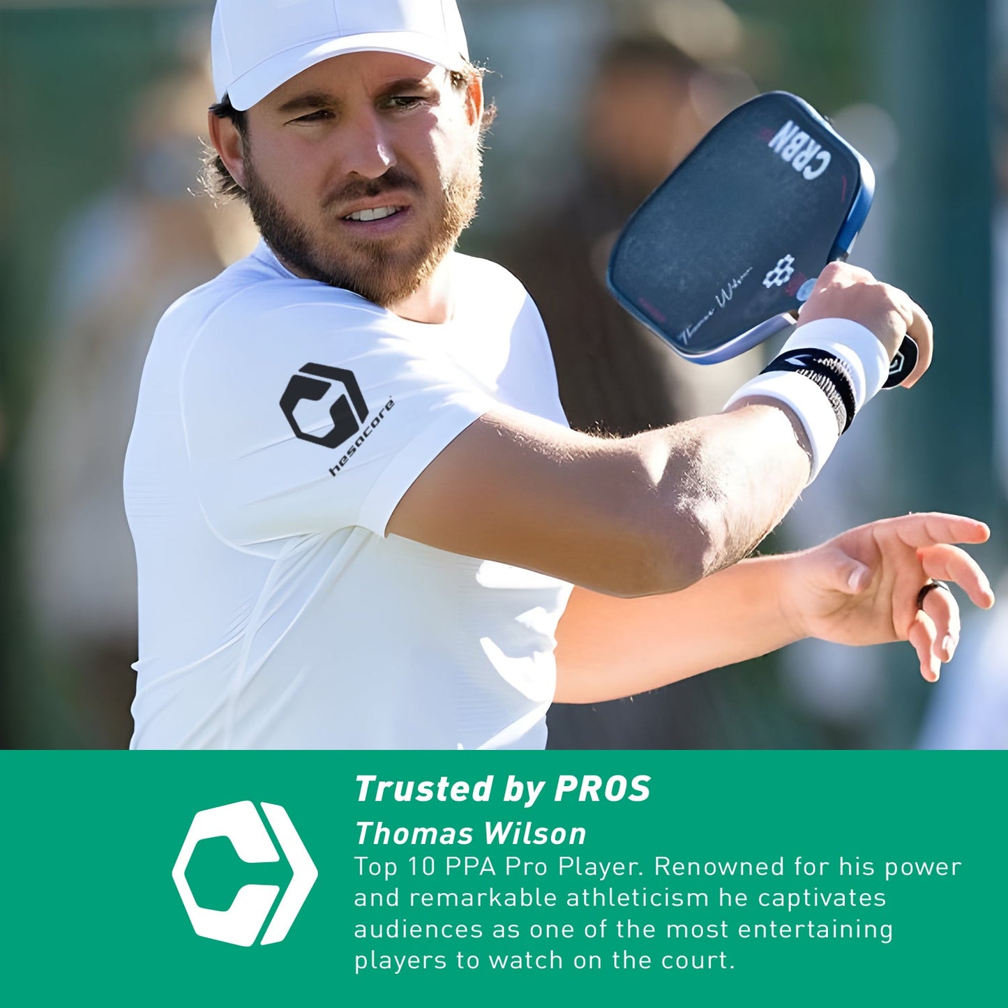 A top PPA pro player named Thomas Wilson, wearing a white cap and shirt, plays pickleball holding a CRBN-branded paddle with the Hesacore Original (White) Pickleball Grip.