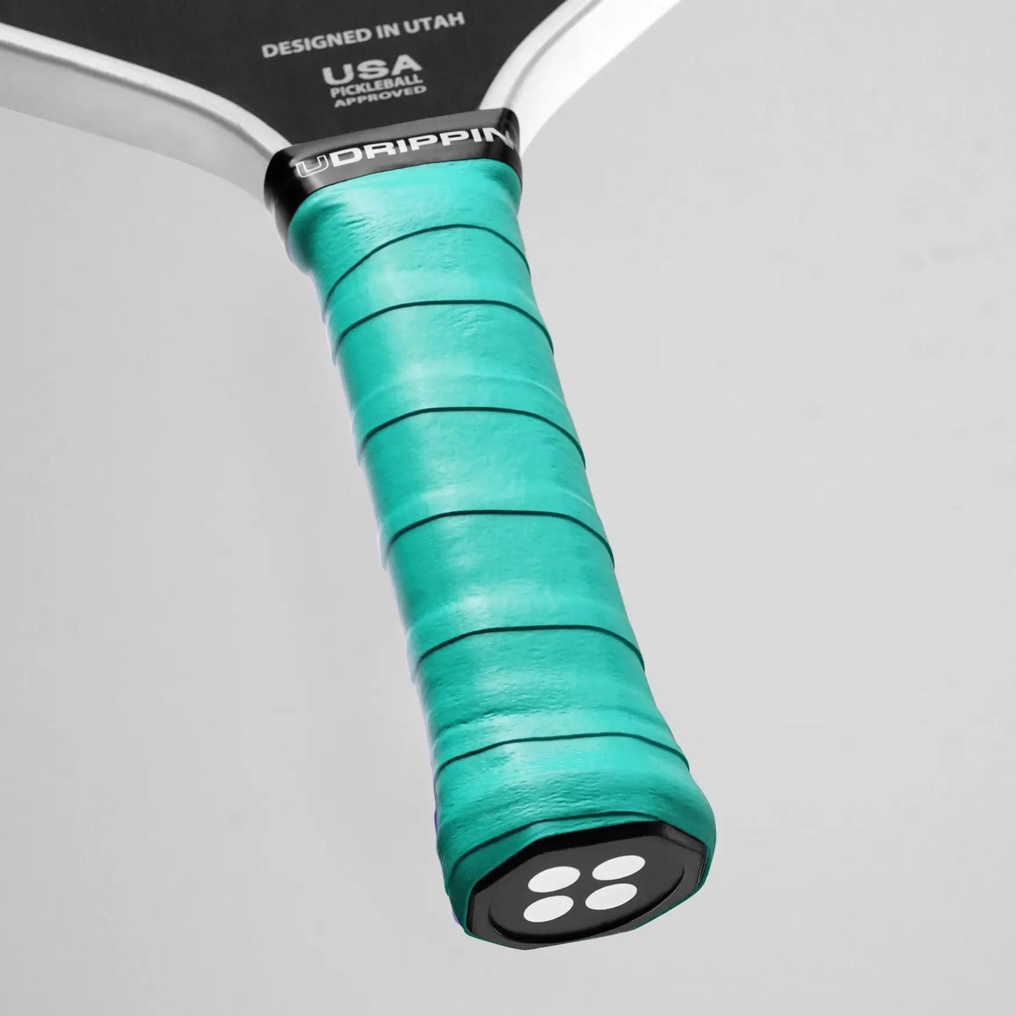 Close-up of a pickleball paddle handle wrapped with a UDRIPPIN Comfort Tour Overgrip in turquoise, featuring the text "USA Pickleball Approved" and "Designed in Utah.