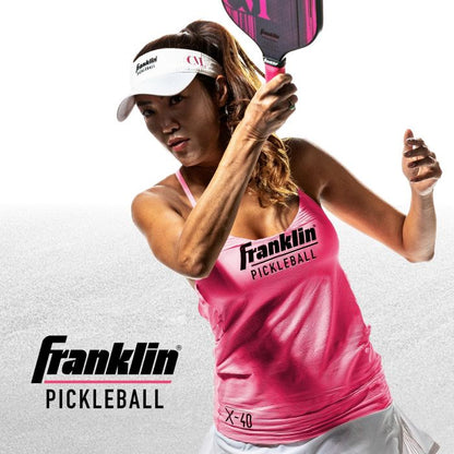 A female athlete wearing a pink tank top and visor, playing pickleball, holding a Franklin Christine McGrath Signature Pickleball Paddle with a focused expression. Pickleballist logo visible.