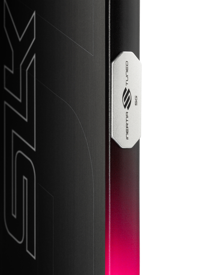 Close-up of a metallic Selkirk badge on a black and pink gradient surface, highlighting the Selkirk SLK GEO Widebody 14mm Pickleball Paddle with partial stylized text—a tribute to its widebody design.