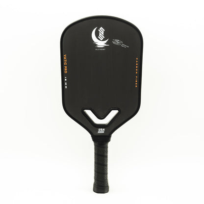 A black pickleball paddle with "Vatic Alchemy 13.5mm," "CARBON FIBRE," and the brand's logo printed on the face, featuring a textured grip handle.