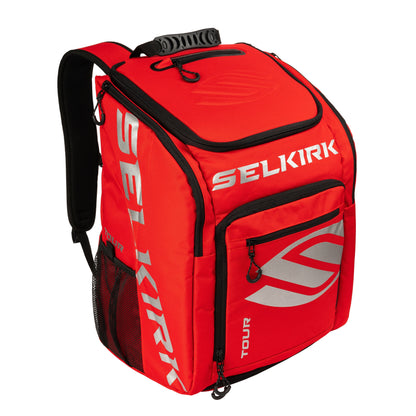 A red and black Selkirk Core Series Tour Backpack Pickleball Bag with multiple compartments, including a front zippered pocket and side mesh pocket, designed for sports or travel use.