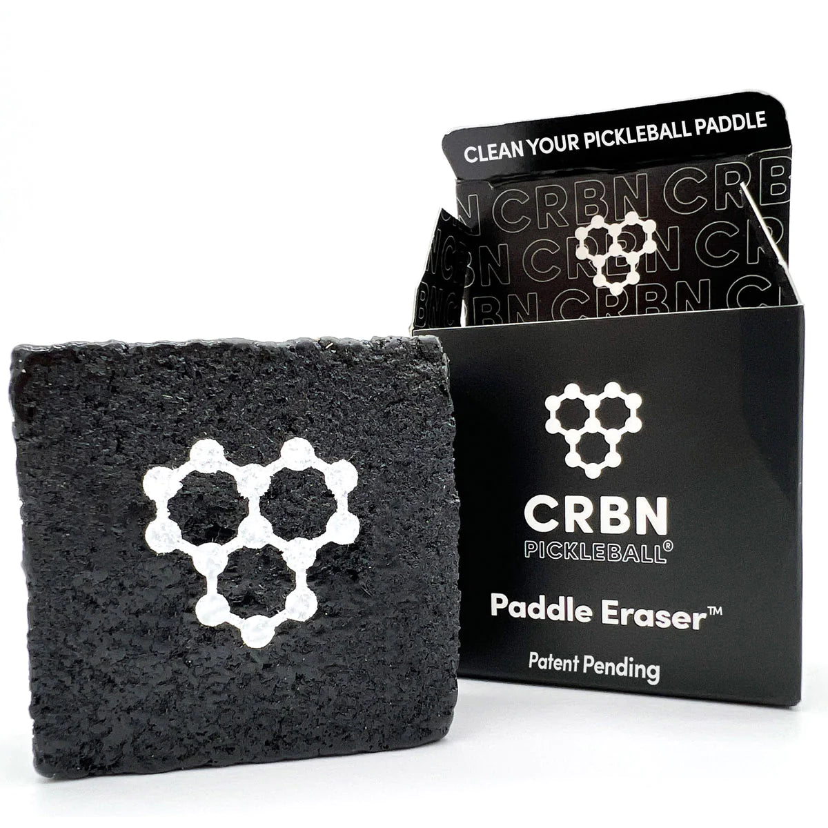 CRBN Pickleball Paddle Eraser shown with its box. The CRBN eraser is black with a white molecular design on its surface. Text on the box reads "Clean Your Pickleball Paddle" and "Paddle Eraser™.