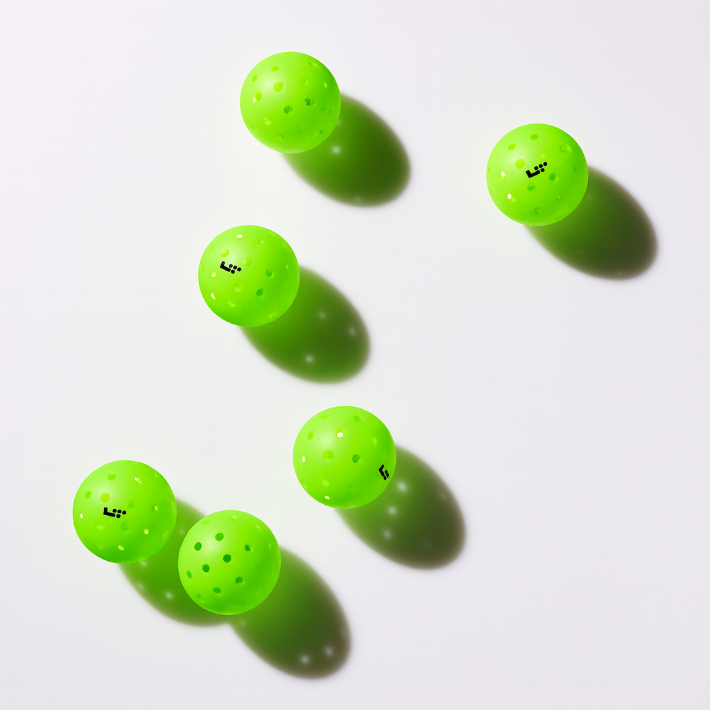 Six Life Time LT Pro 48 Pickleball Balls by Life Time are arranged on a white surface, each bright green and perforated, casting distinct shadows—a vibrant and eye-catching display.