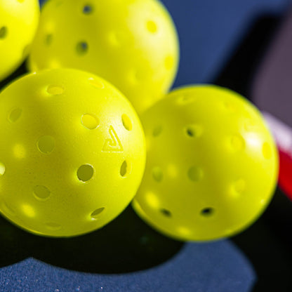 Close-up of several Pickleballist JOOLA HC-40 Pickleballs in Shock Yellow, recognized for their tournament durability, scattered on a dark surface.