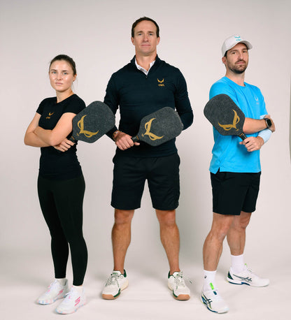 Three people in athletic wear stand side by side, each holding an OWL CXE - Drew Brees Limited Edition Quiet Pickleball Paddle by OWL, facing the camera against a plain background.