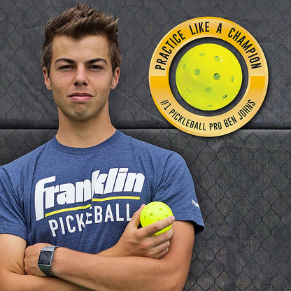 Young man holding an Franklin X-40 Outdoor Pickleball Ball with machine-drilled holes, wearing a Pickleballist pickleball t-shirt, with a logo saying "practice like a champion" featuring a pickleball and text "#1 Pick