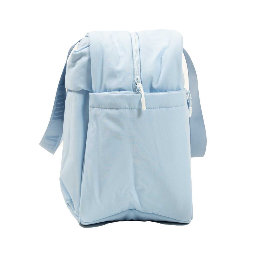 The JOOLA Overnighter Puff Bag by JOOLA is a light blue rectangular shoulder bag featuring a quilted design, zipper closure, exterior pocket, and adjustable strap, shown standing upright on a white background.