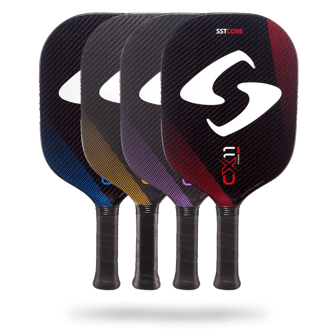 Four colorful Gearbox CX11 Quad Pickleball Paddles with black handles are displayed in a row, each paddle showcasing a different accent color: blue, yellow, purple, and red. Designed with the advanced SST ribbed core and CX11 Quad Control technology, these paddles offer a larger sweet spot for improved precision.