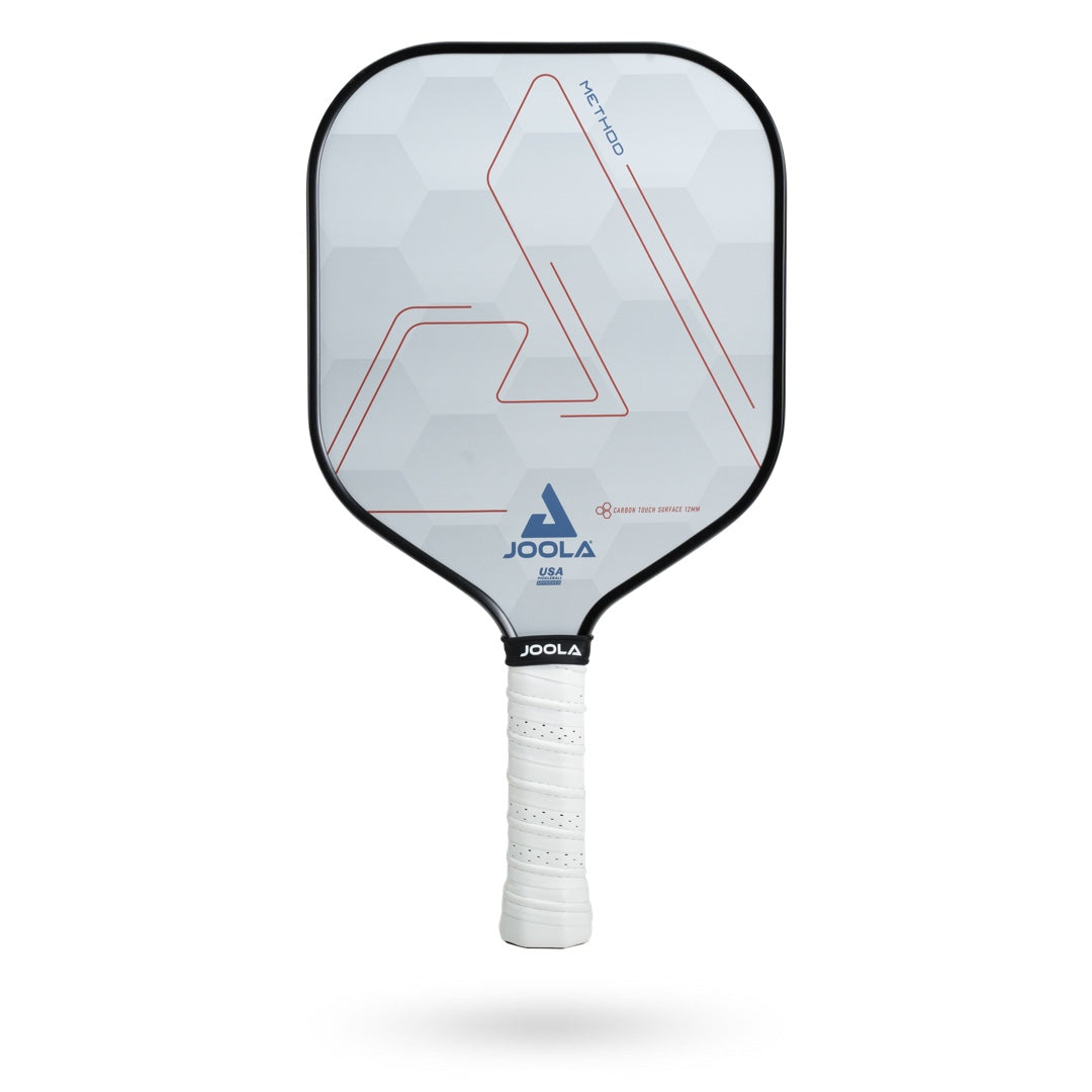 A white JOOLA Method CTS 12 Pickleball Paddle with a geometric hexagon design, red lines, and the JOOLA logo in blue and black. The handle is wrapped in white grip tape. This paddle features a honeycomb polymer core for superior performance.