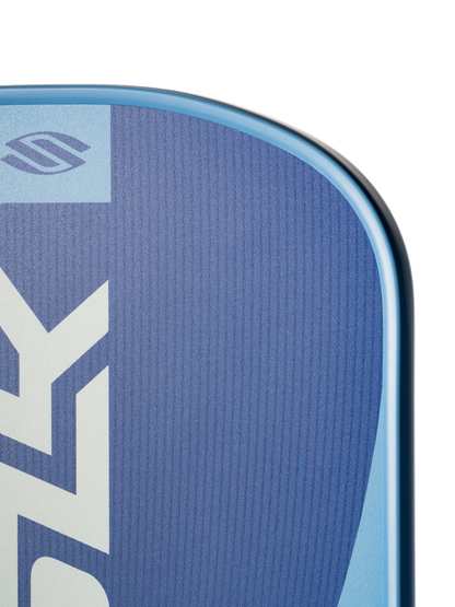 Close-up of the top corner of the Selkirk SLK Valkyrie Widebody 16mm Pickleball Paddle featuring a blue surface, smooth curved edge, and white geometric patterns.