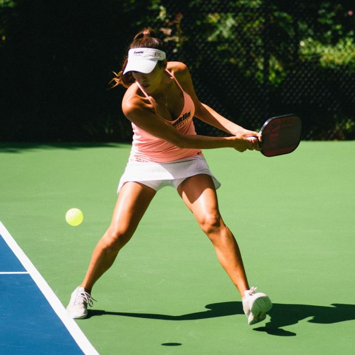 A woman hitting a Franklin Christine McGrath Signature Pickleball Paddle on a tennis court.