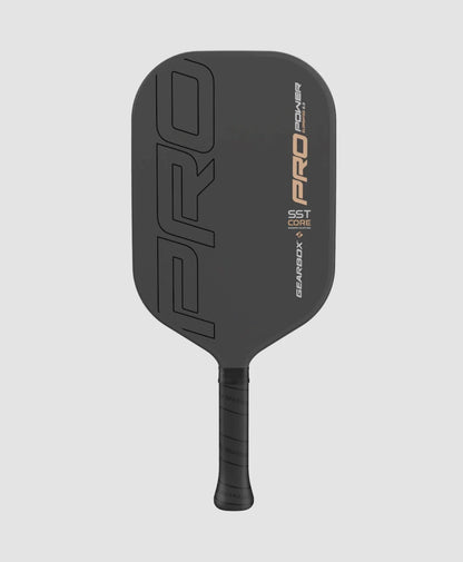 Image of a black pickleball paddle with "PRO" prominently printed on the surface, featuring a carbon fiber framework and "Gearbox Pro Power Elongated Pickleball Paddle" along the side. The handle is wrapped in black grip tape.