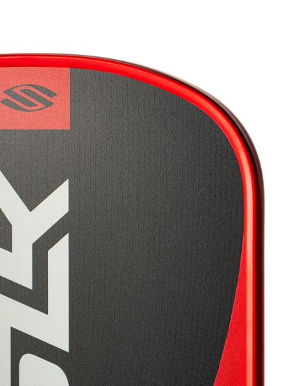 Close-up of the top corner of a Selkirk SLK Valkyrie Widebody 16mm Pickleball Paddle, featuring a red edge, black and gray surface, and partial Selkirk logo.