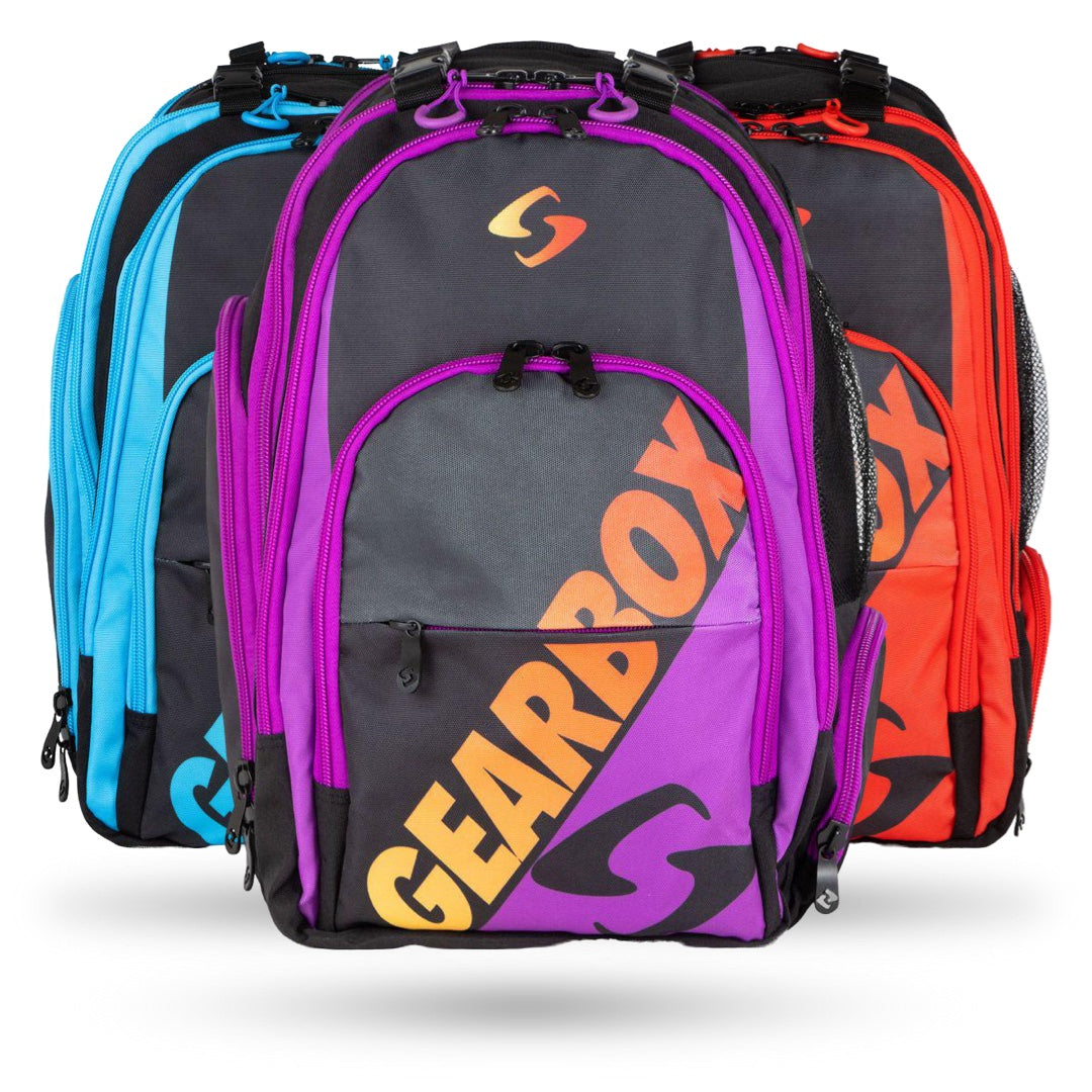 Three Gearbox Court Backpack Pickleball Bags by Gearbox in blue, purple, and red with black and orange accents are displayed side by side. These durable and practical backpacks feature spacious compartments ideal for all your needs.