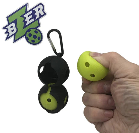 A hand squeezes a small yellow BZER Mini Training Pickleball, while a black holder with two balls and a ball bag clip is shown. "Bzer Sports" logo appears in the top left. Product: BZER Mini Training Pickleball (2 balls + Ball Bag Clip).