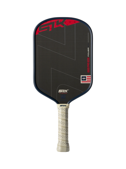 The Selkirk SLK ERA Power Elongated Carbon Fiber Pickleball Paddle by Selkirk features a sleek black elongated design, a beige perforated grip, red and white graphic accents, and a small American flag detail on the lower right corner of the paddle face.